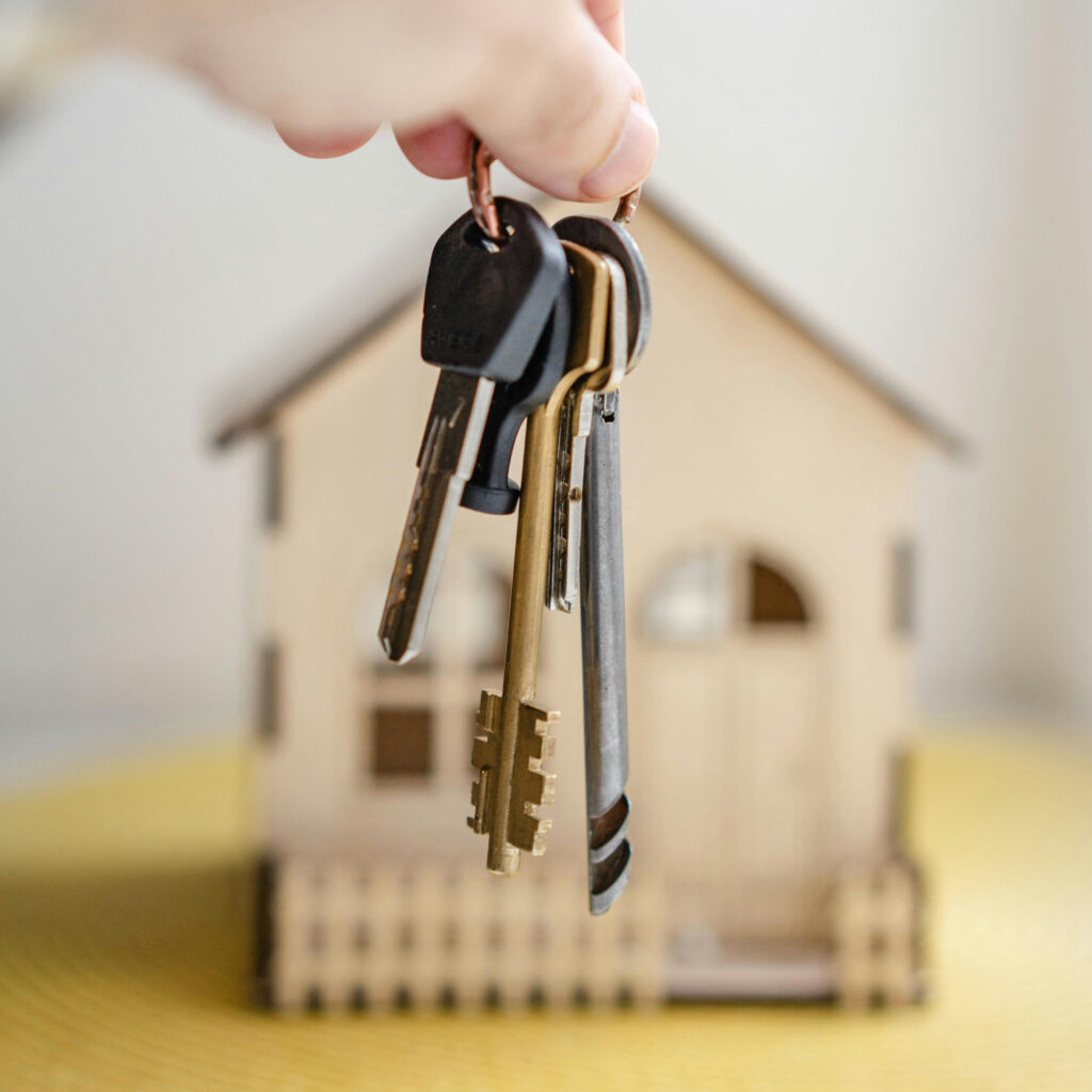 Holding keys in front of a wood model house to express the idea of becoming a homeowner.