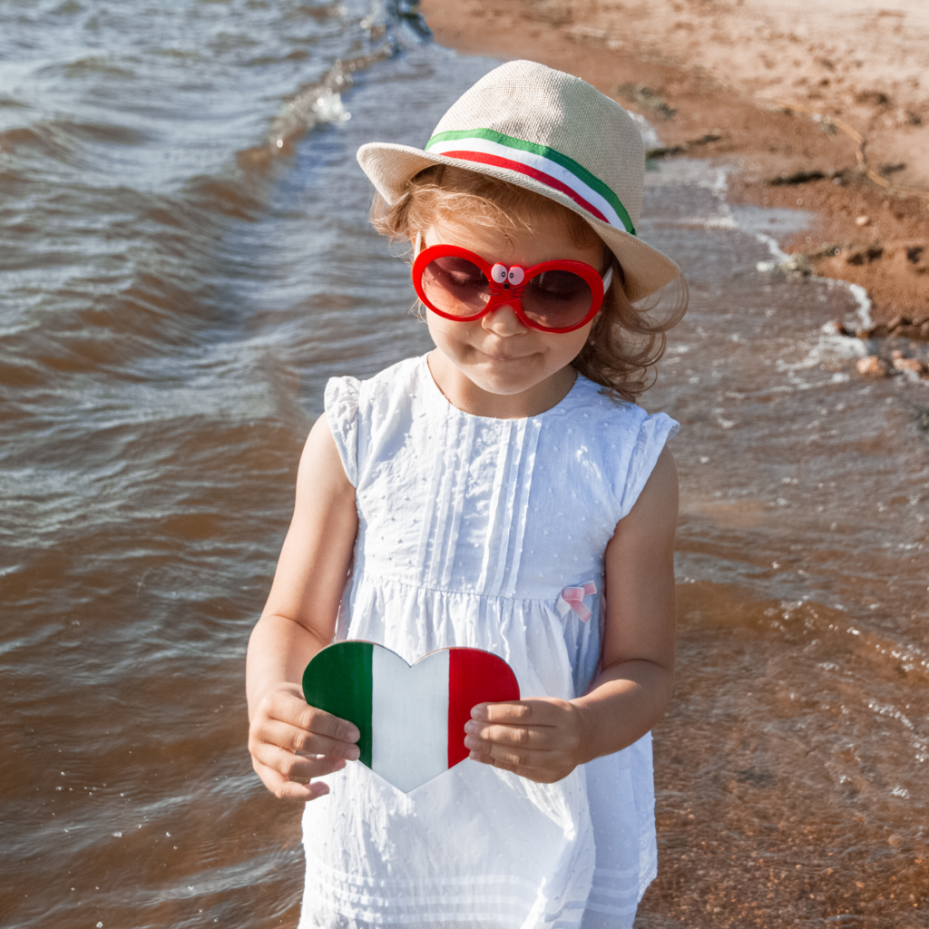 Little girl holding heart shaped Mexican flag at the beach.